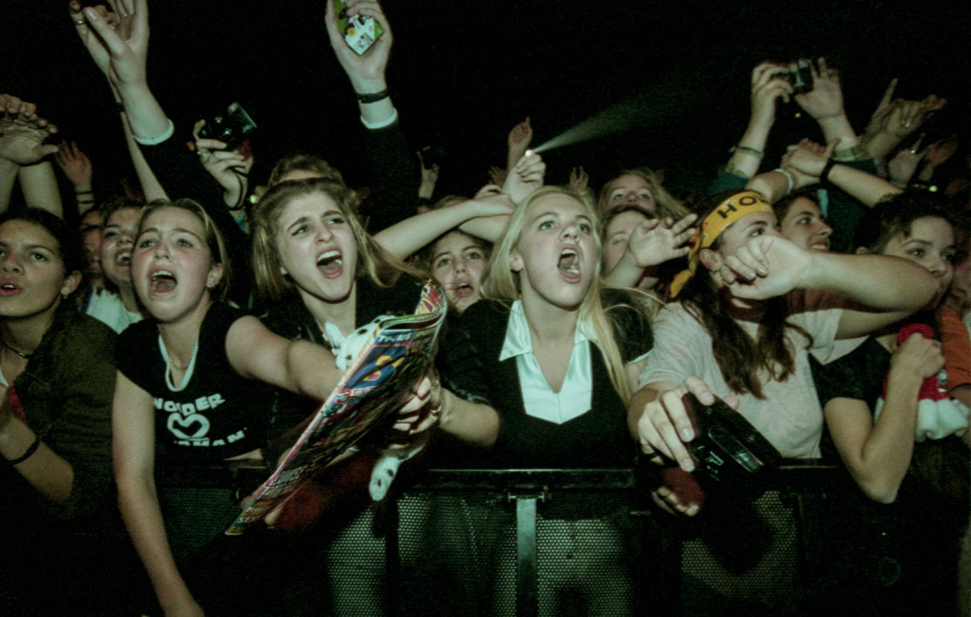 fans in the front rows of the audience, cheering, screaming and holding banners while watching American boyband Backstreet Boys. (Photo by Paul Bergen/Redferns)